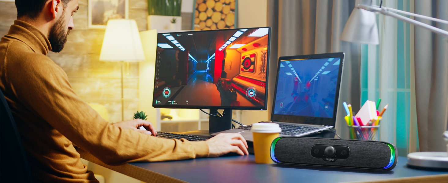 Gaming or work setup featuring multiple monitors, laptop, and illuminated peripherals on desk with warm ambient lighting.