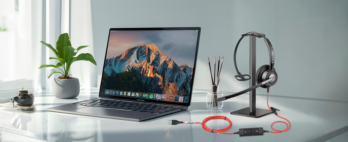 Modern desk workspace with laptop displaying mountain wallpaper, microphone setup with headphones, and small potted plant against blue-gray wall.