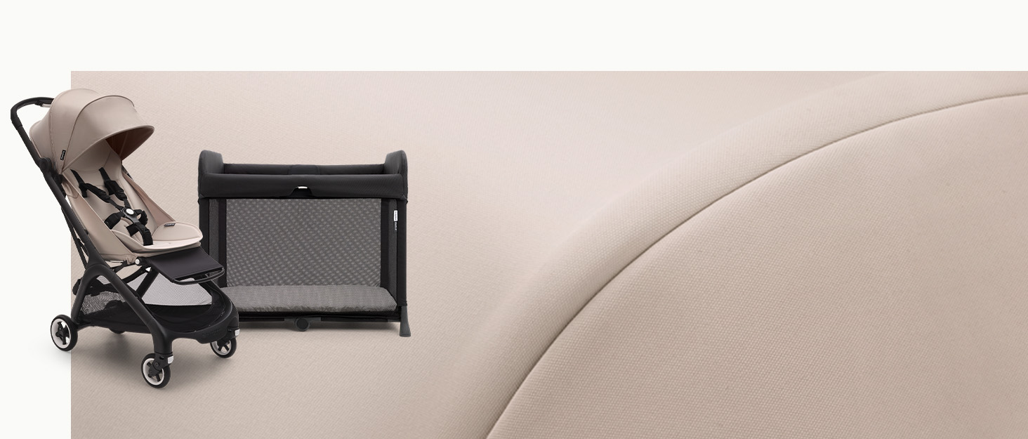 Compact folding baby stroller in beige color next to a portable play yard or travel crib with mesh sides, positioned on a light-colored sofa or couch.