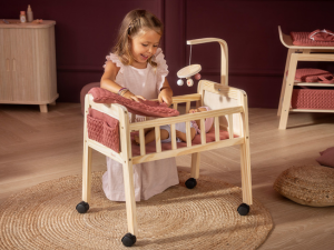 Child playing with white wooden doll crib or bassinet on wheels in playroom setting.