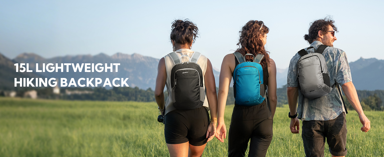 Three people wearing hiking backpacks viewed from behind, standing on trail overlooking mountainous landscape.