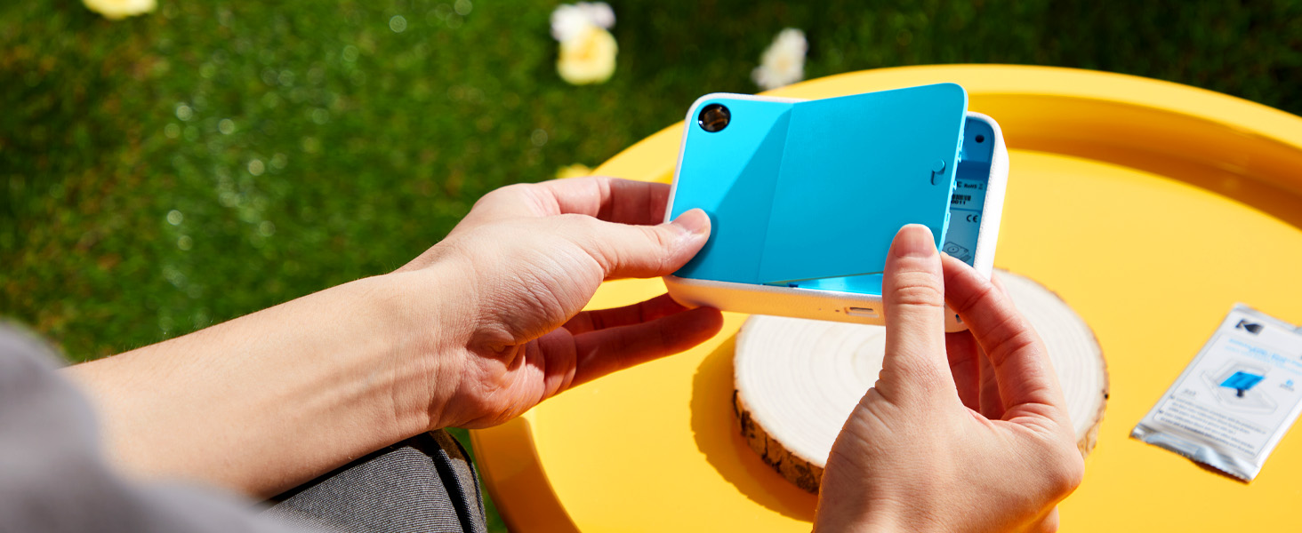 Closeup shots of hands interacting with yellow smartphone or device against outdoor grass background.