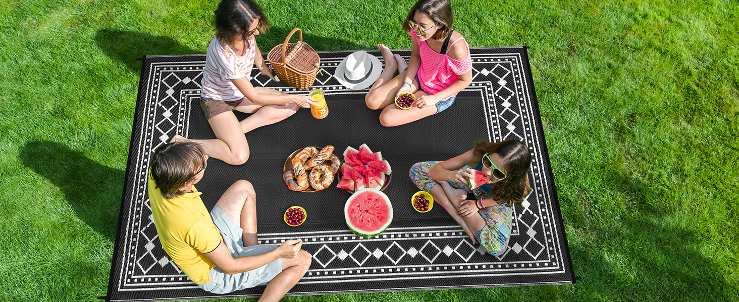 Group gathered outdoors on a patterned picnic blanket, enjoying a casual meal together.