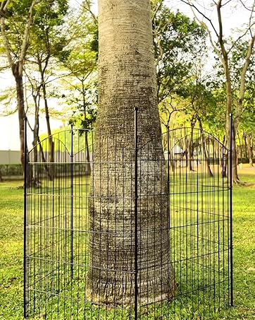 Metal fence panels arranged in circular formation around large tree trunks in grassy parkland setting. Multiple panels shown from different angles.