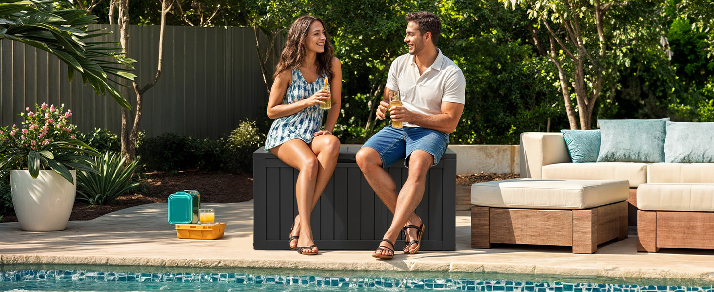 Outdoor patio scene with people relaxing on lounge furniture. Pool or water feature visible in background.