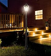 Two decorative lamp posts illuminating wooden park benches against a stone wall backdrop with green foliage at night.