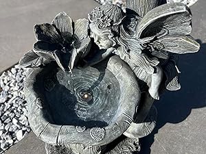 Decorative garden fountain featuring a detailed fairy or angel figure perched on a tiered stone basin structure.