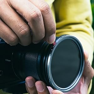 Close-up of camera lens with purple-tinted filter or protective glass, showing textured grip surface and red indicator dot.