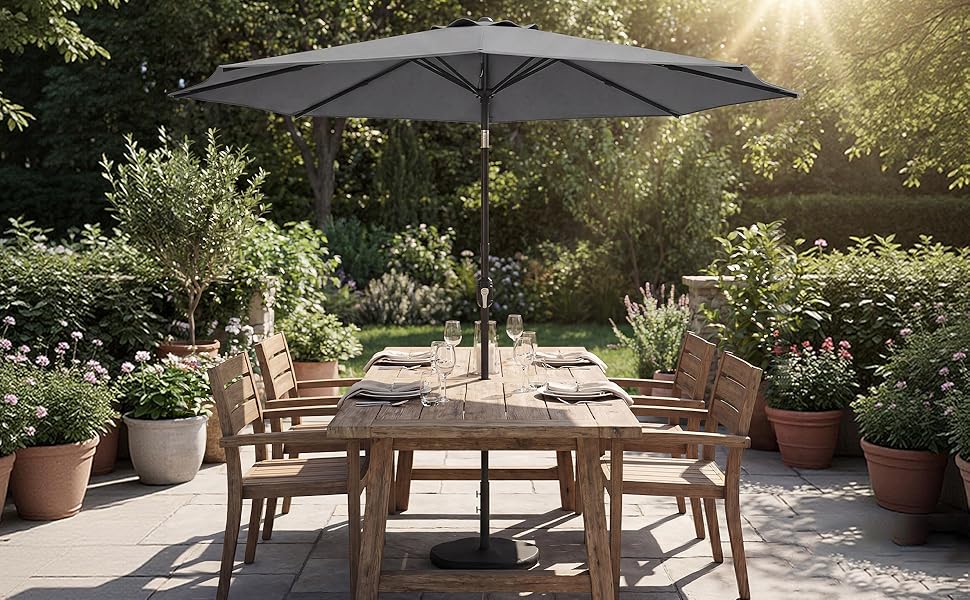 Outdoor patio setting with wooden furniture including tables and chairs under large umbrellas, set against lush garden backdrop with natural sunlight filtering through.