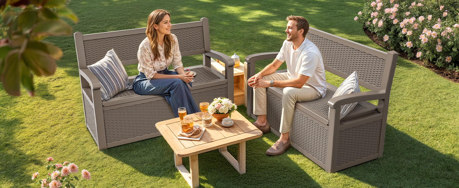 Outdoor patio scene with two wicker-style chairs and matching coffee table on lawn. Table set with refreshments, garden setting with roses in background.