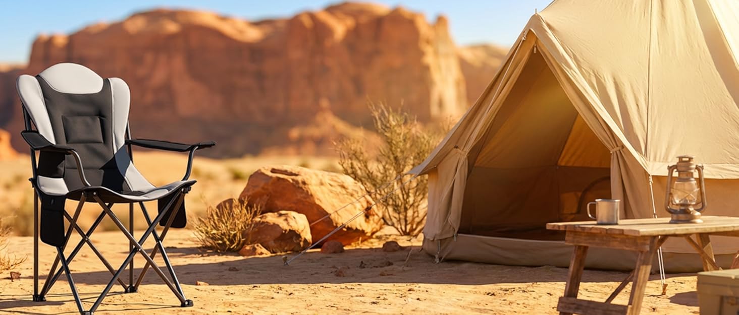 Desert camping scene featuring black folding camp chair with white accents positioned on sandy ground, tan canvas tent in background, rocky desert formations visible under clear sky.