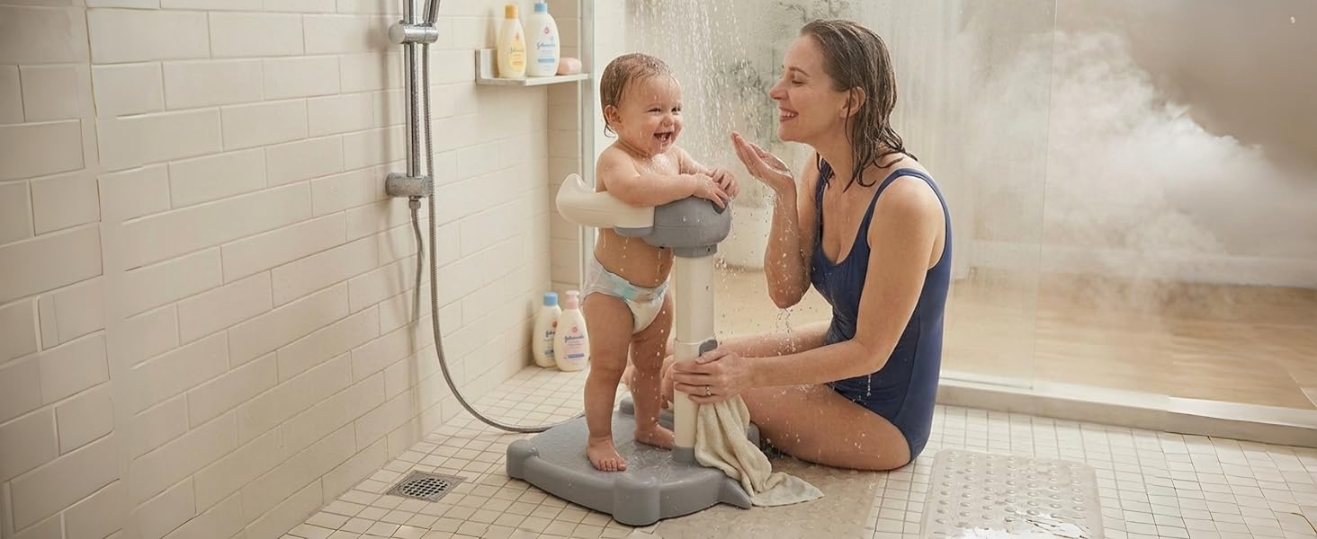 Woman and infant in bathroom with shower fixtures visible. Steam present. Woman holding child near shower area with white tile walls.
