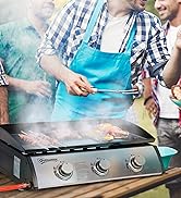 Portable gas grill with two burners and griddle cooking surface, actively cooking meat and vegetables. Person using tongs at outdoor gathering with guests and food table visible in background.