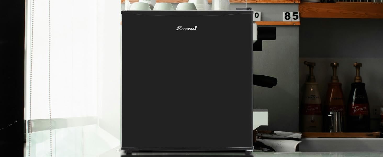 Compact black mini refrigerator shown in kitchen setting with bottles visible in background.