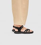Person wearing brown A-line skirt with black and tan strappy sandals featuring thick rubber soles, displayed from waist down on white background.