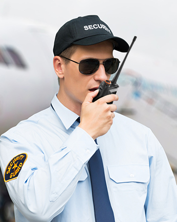 Construction worker wearing white hard hat and blue uniform, using handheld radio. Close-up profile view showing safety equipment and communication device.