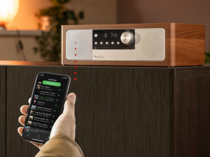 Text reads 'PREMIUM ALL-IN-ONE MUSIC SYSTEM'. Lifestyle image showing a modern speaker system in a cozy home setting with warm lighting and decor.