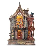 Two-story miniature wooden house model with dark roof, cream-colored walls, illuminated windows, detailed furnishings visible inside both levels, small red accessories and landscaping elements at base.