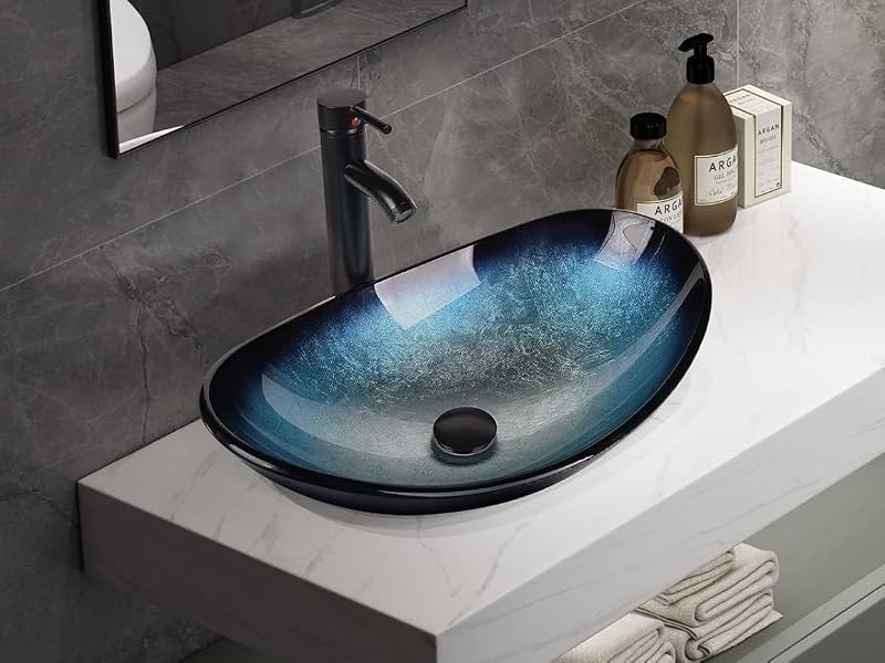 Modern bathroom vanity with white countertop and blue oval sink. Features black faucet, wall-mounted mirror, and decorative items on countertop. Set against a grey textured wall.