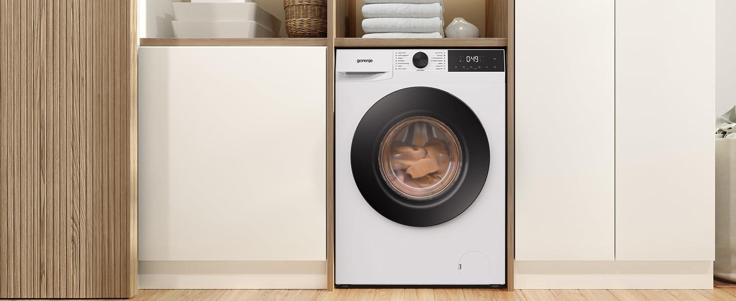 Front-loading washing machine with white body and black circular drum, positioned next to cream cabinetry in modern laundry room setting with wooden accents.