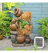 Decorative garden water feature showing terracotta-colored figures arranged beside a solar panel, with green foliage and blue wall in background.