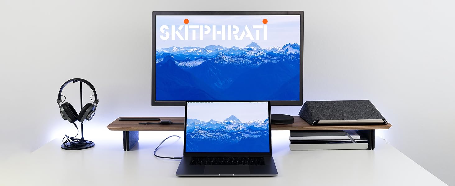 Desktop workspace showing laptop and monitor displaying blue mountain landscape imagery, with desktop fan and storage boxes on white desk setup.