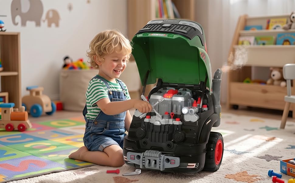 Toddler playing with green and black wheeled toy tool chest indoors in playroom with colorful rug, storage shelves, and toys visible in background.