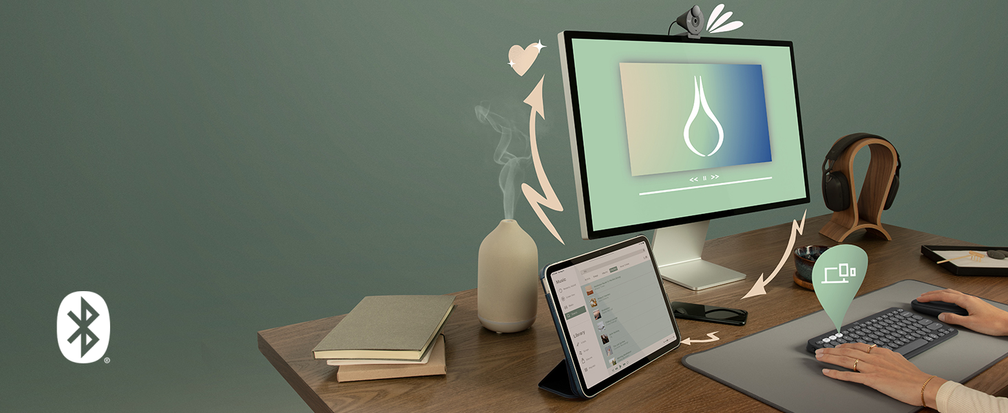 Desk workspace styled with computer monitor displaying pendant light design, wireless earphones, notebook, pen, succulent plant, and Bluetooth icon symbol on green wall background.