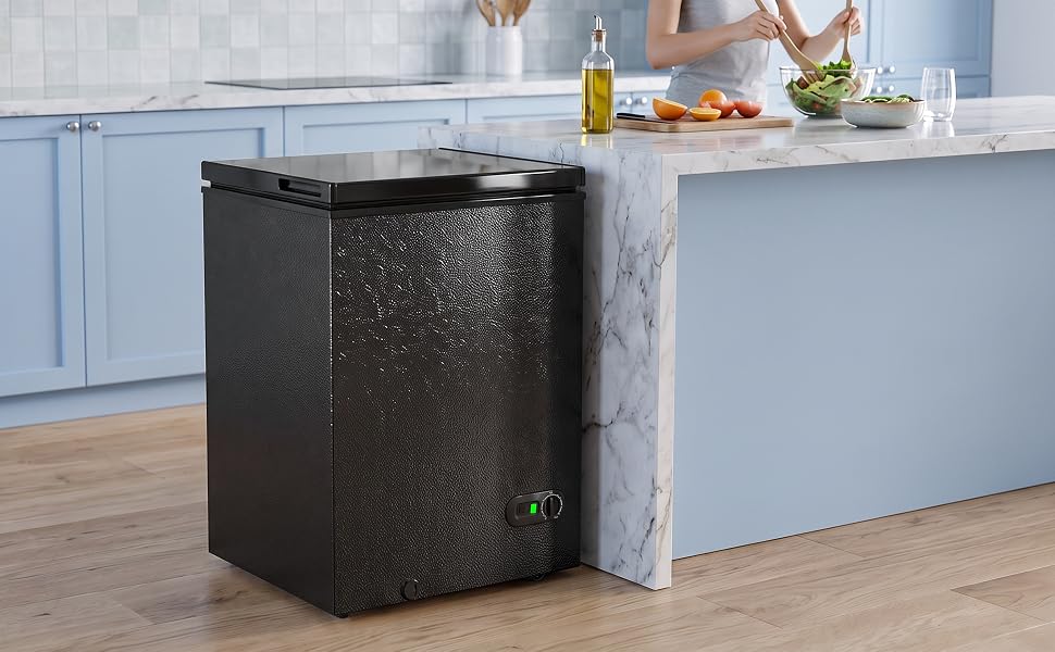 Black upright trash bin with flip-open top positioned beside kitchen island. Sleek waste container with modern minimalist design for kitchen countertop or workspace waste management.
