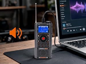 Handheld digital radio transceiver with display screen and antenna, positioned next to laptop showing audio waveform software, orange speaker visible on workspace desk.