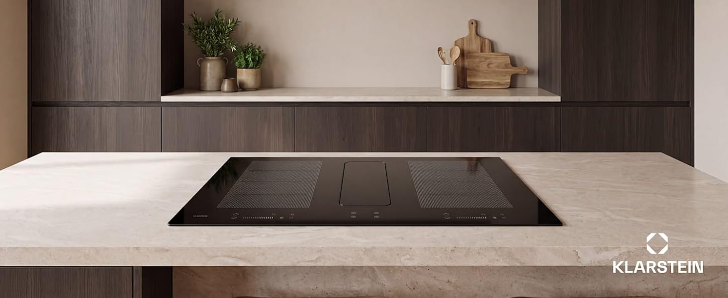 Modern kitchen interior with black rectangular cooktop/range installed in white counter, dark cabinetry above, minimalist design with plant and accessories visible.