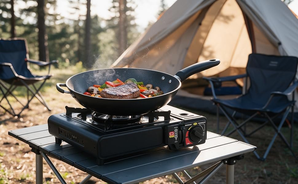 Outdoor dining setup featuring black circular grill/cooktop with grilled meat and vegetables, placed on table with beer bottles and dishware in garden setting with string lights and trees.