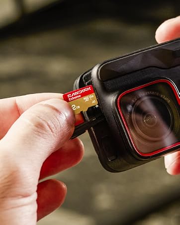 Text reads 'At Sandisk, we keep people and businesses moving forward with inspired innovations to actualize their potential.' Hands holding device near backpack with red accents.