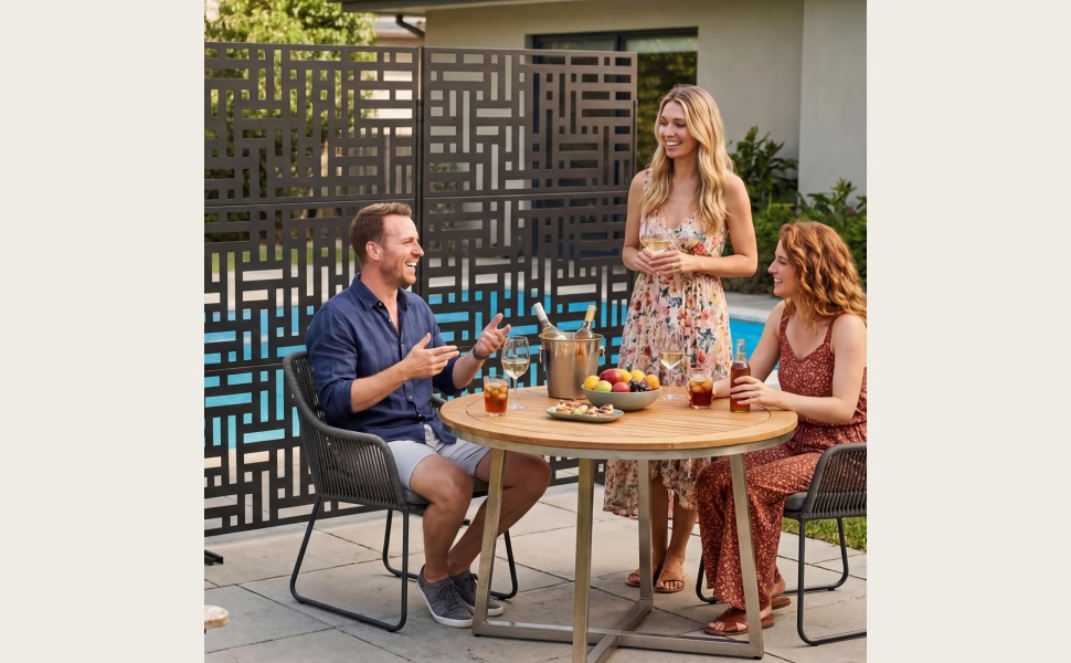 Black geometric maze or lattice pattern privacy screen panel displayed outdoors on patio furniture with garden and flowering plants visible in blurred background.