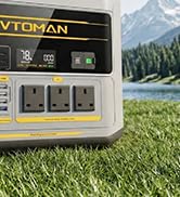 Small grey charging station or device box mounted outdoors on grass, featuring a compact design with a dark screen display.