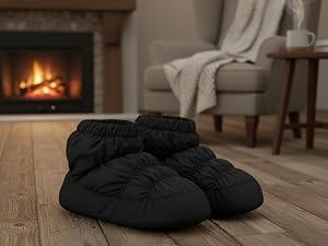 Pair of black quilted puffer slippers photographed on white textured surface, featuring gathered fabric design and soft appearance for indoor wear.