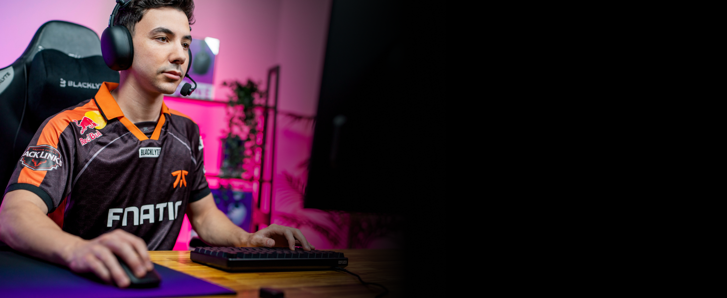 Dark room with multiple people sitting at computer stations in a row, illuminated by screen light