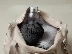 Beige canvas tote bag displayed open, revealing black interior compartment structure and capacity.